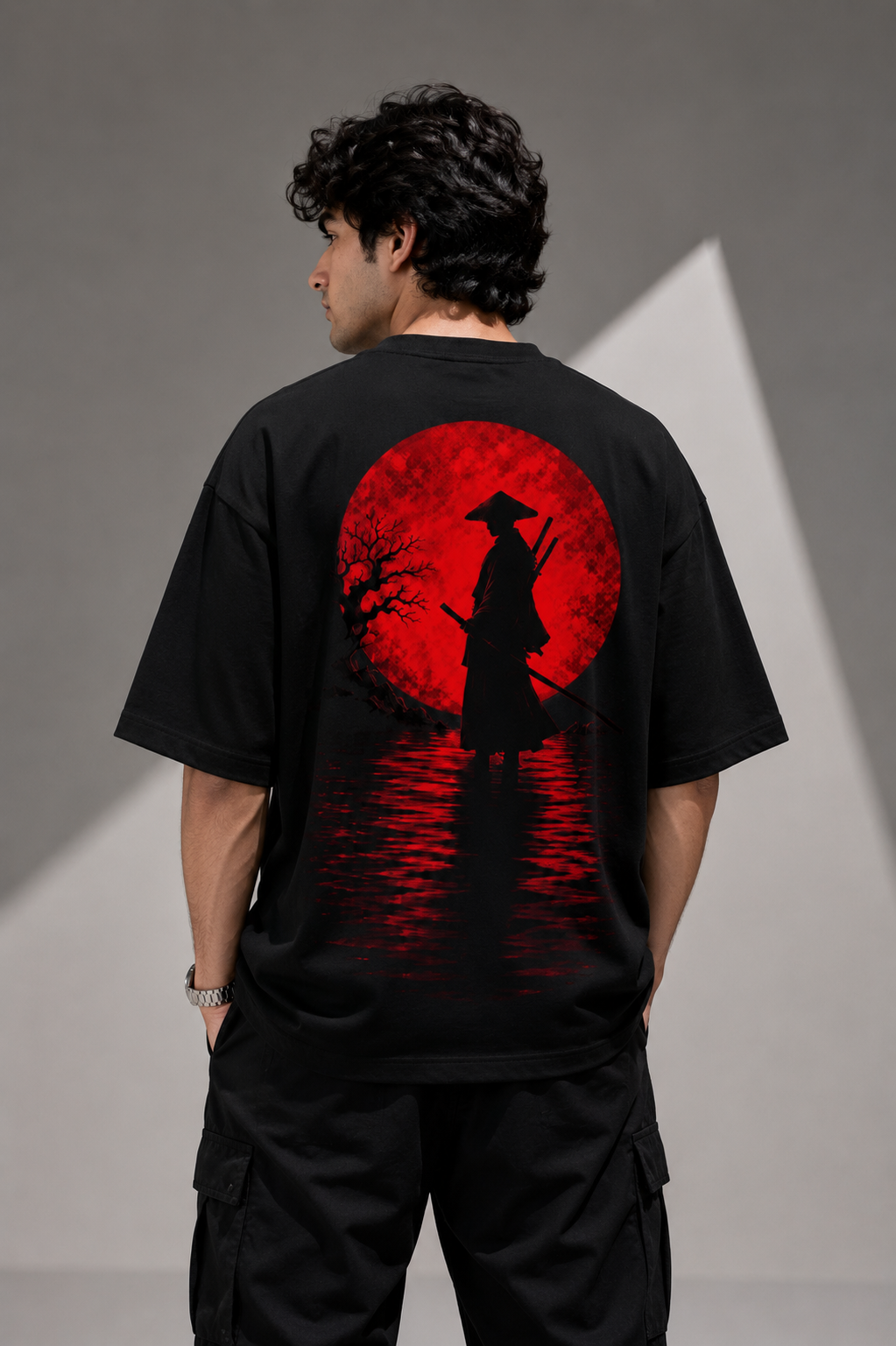A man wearing a black oversized t-shirt with a large red graphic print on the back, featuring a silhouette of a samurai standing in front of a red full moon over water.