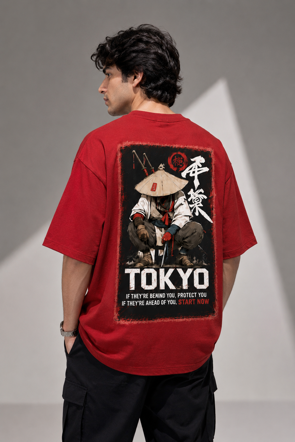A man wearing a red graphic t-shirt, viewed from the back. The shirt features a large black rectangular graphic print with a samurai illustration, Japanese characters, and the text 'TOKYO' and 'IF THEY'RE AHEAD YOU, START NOW'.