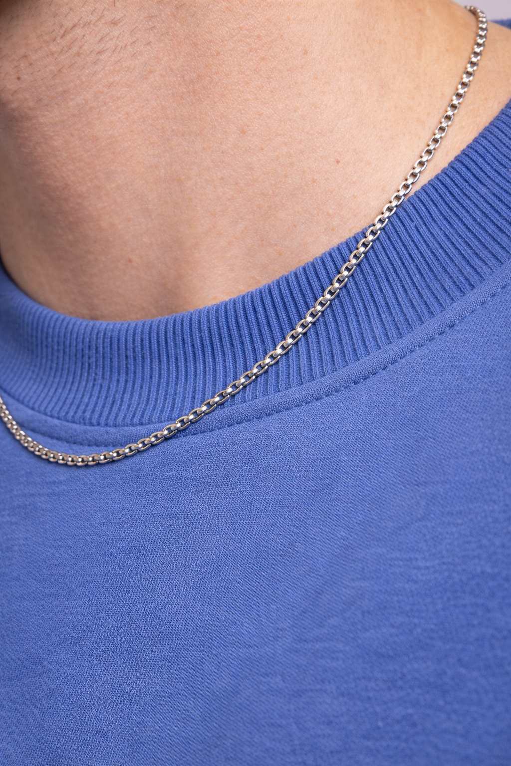 Close-up of a person wearing a blue sweater with a silver chain necklace.