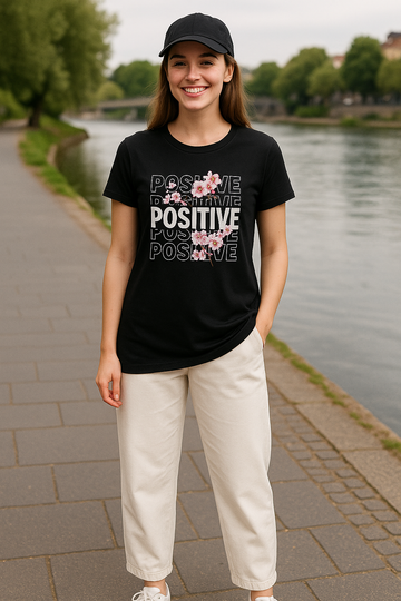 "Front view of woman wearing AUA&CO skirt-style black positive t-shirt with white cotton trousers – summer streetwear look"