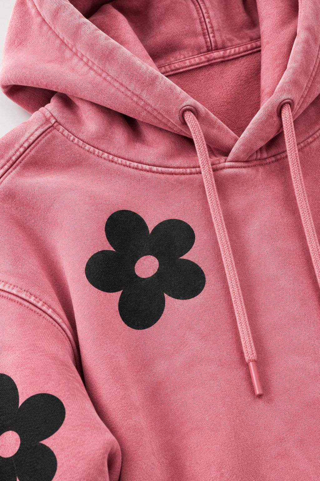 Close-up of AUA&CO pink dye-washed fleece hoodie showing fabric texture, detailed stitching, drawstrings and black floral DTF print