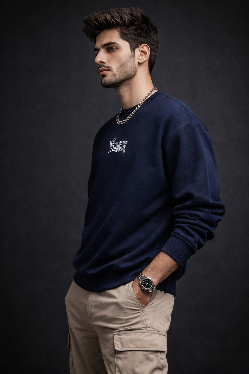 Man wearing a navy blue sweatshirt with a logo, beige pants, and a watch on a dark background