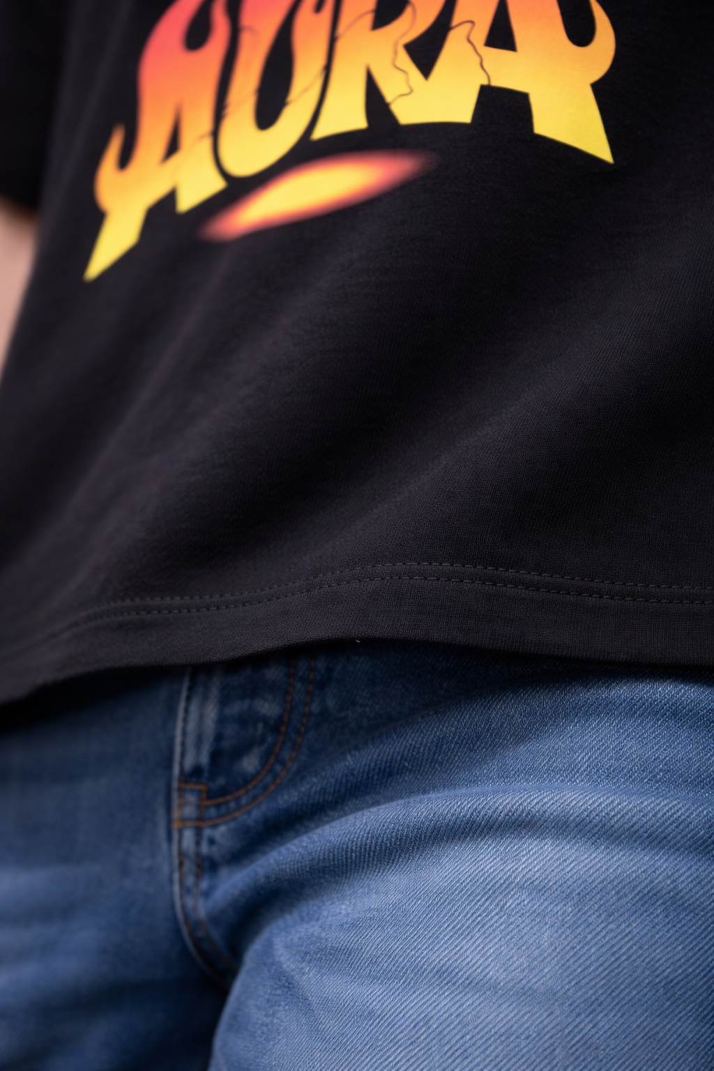 Black t-shirt with 'AURA' printed in yellow and red on a person wearing blue jeans.