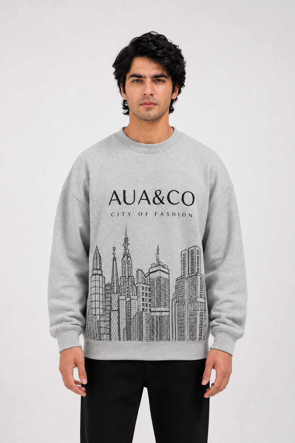 A man wearing a light gray crewneck sweatshirt with a black graphic print of the Kuala Lumpur skyline and the text 'AUA&CO CITY OF FASHION'.
