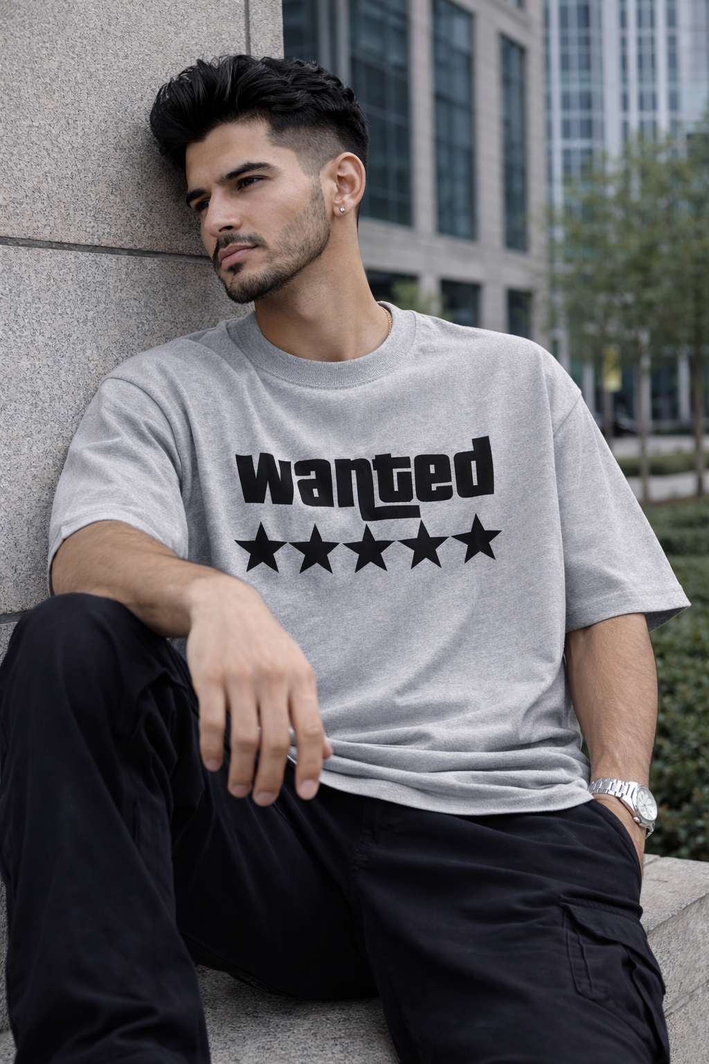 Man wearing a gray t-shirt with 'Wanted' and five stars graphic, sitting against a wall.