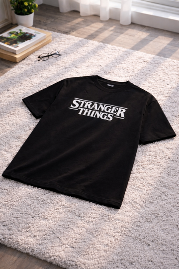 Black t-shirt with 'Stranger Things' logo on a carpeted floor.