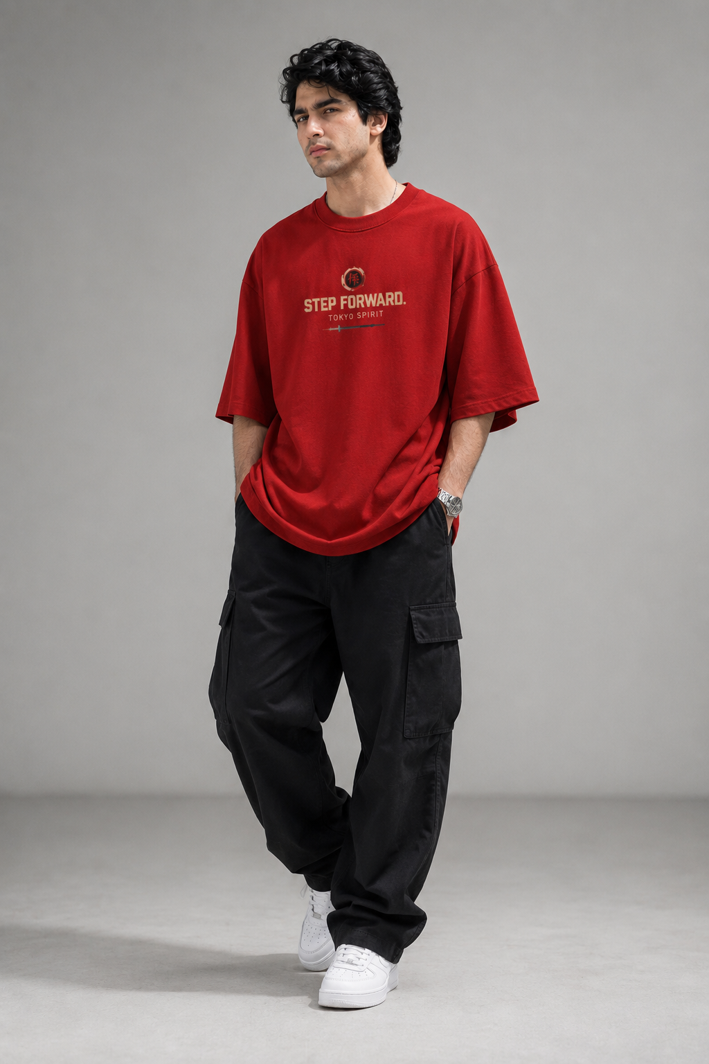 A man modeling an oversized red t-shirt with 'STEP FORWARD.' printed in gold and white on the chest, paired with black cargo pants and white sneakers, against a neutral gray studio background.