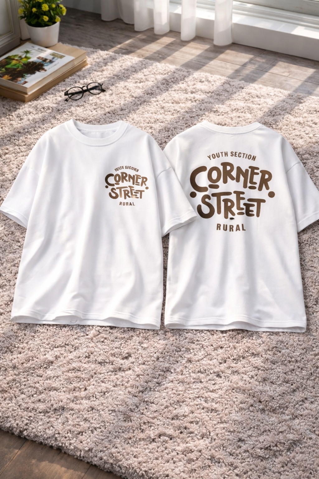 Two white t-shirts with 'Corner Street Rural' print on a carpeted floor.