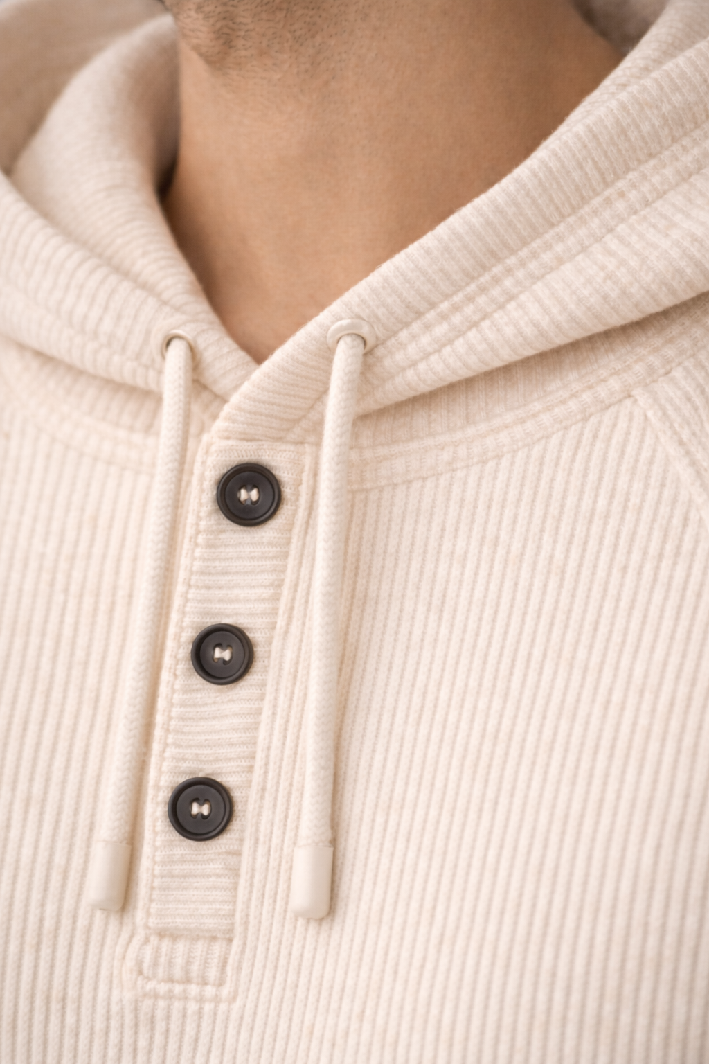 Close-up of a beige ribbed hoodie with buttons and drawstrings.