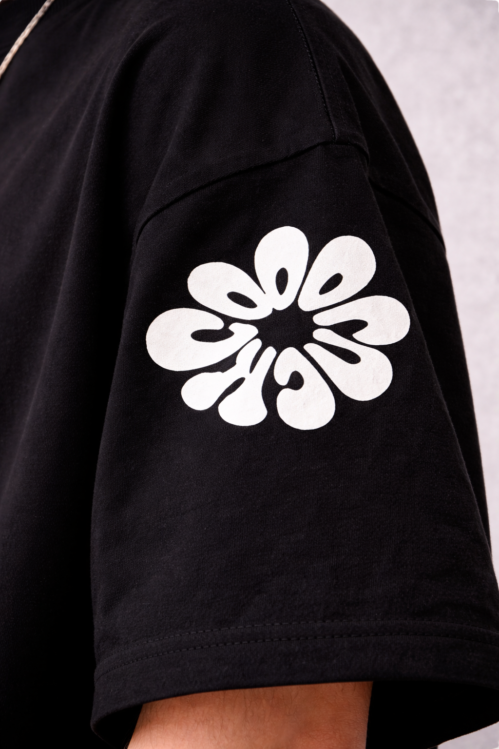 Black t-shirt with a white floral design on the shoulder against a light gray background