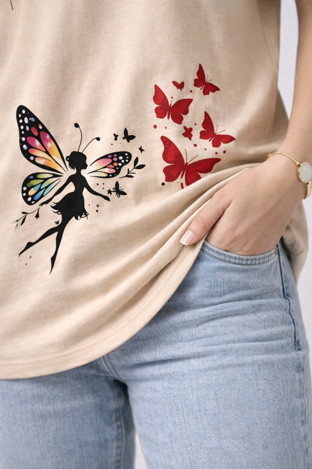 Beige t-shirt with fairy and butterfly designs worn by a person with light blue jeans.