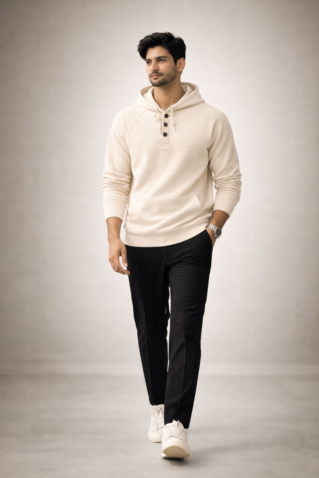 Man wearing a beige hoodie and black pants on a gray background