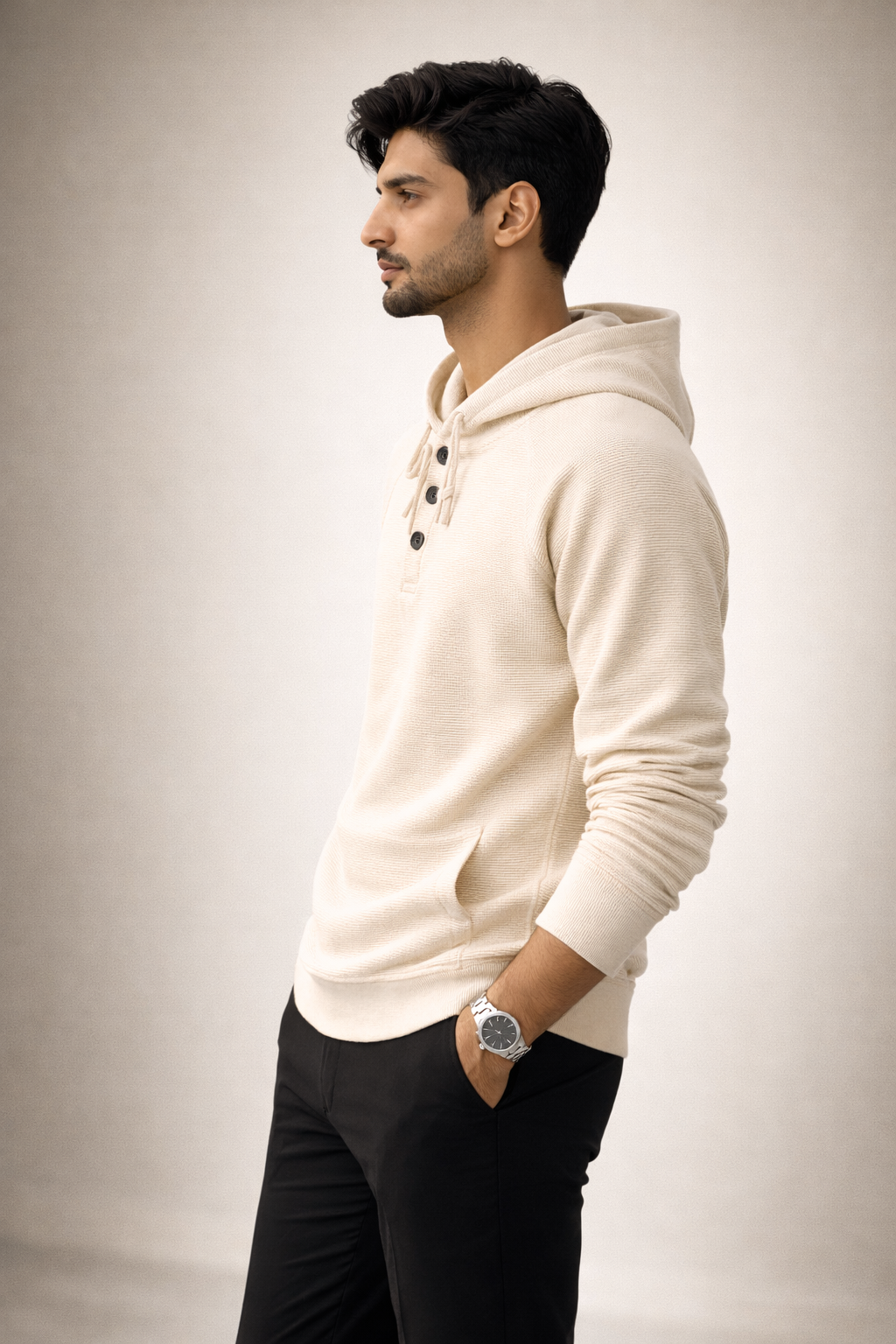 Man wearing a cream hoodie and black pants against a plain background