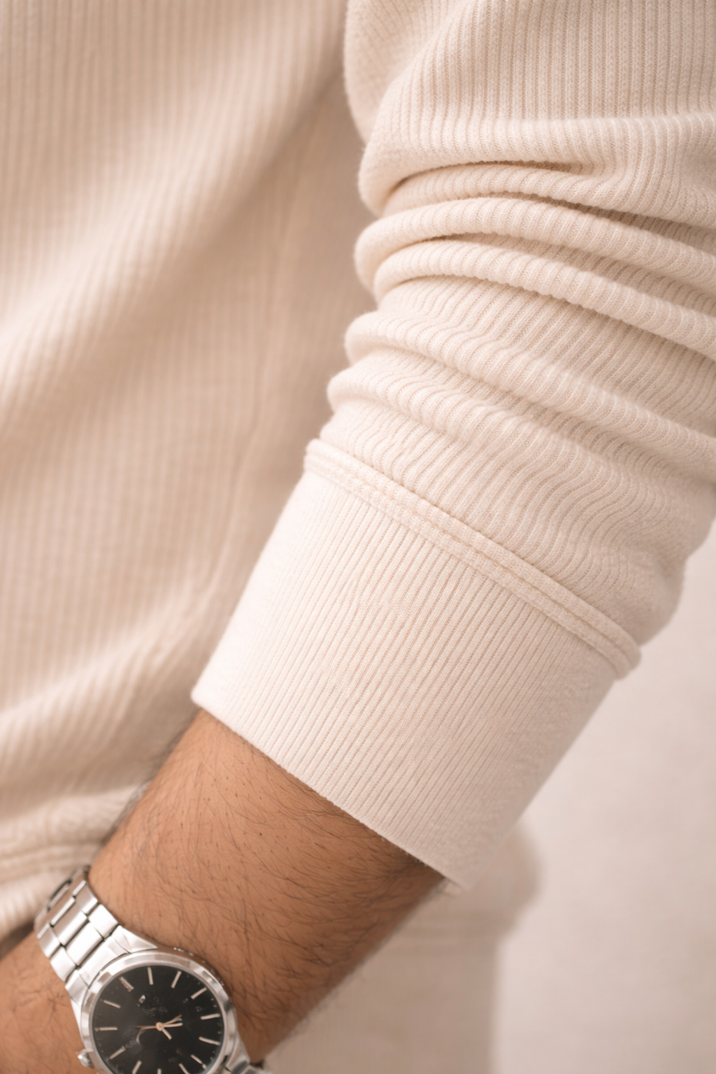 Close-up of a person wearing a silver watch with a beige sweater.
