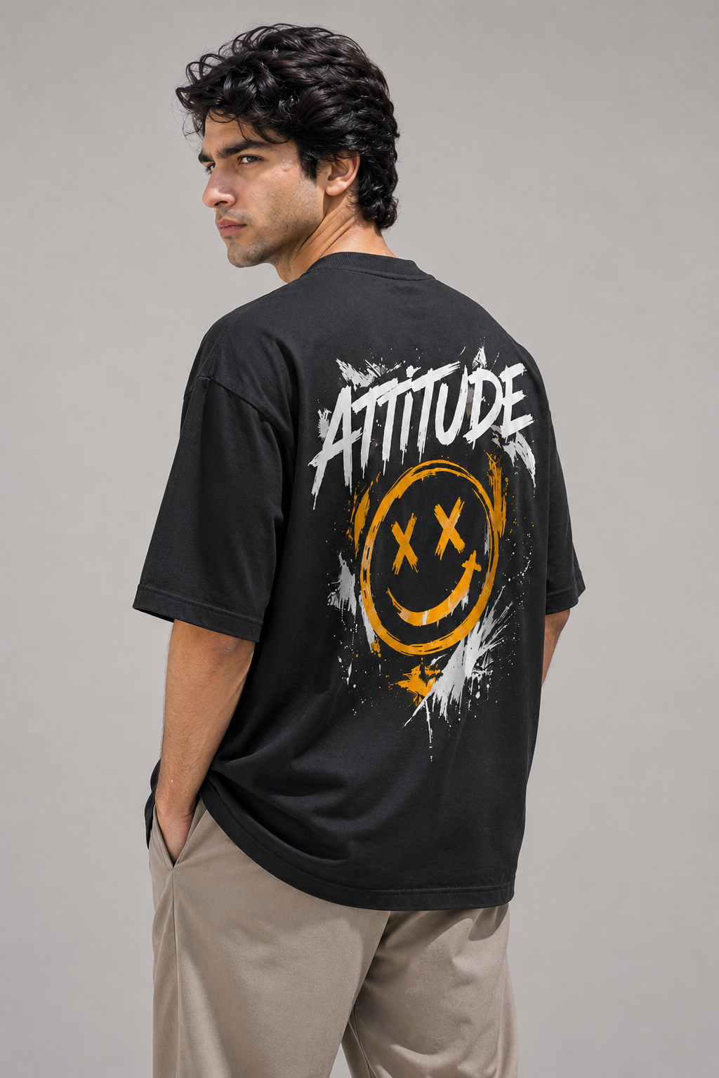 Person wearing a black t-shirt with 'ATTITUDE' and smiley face design on the back, standing against a gray background.