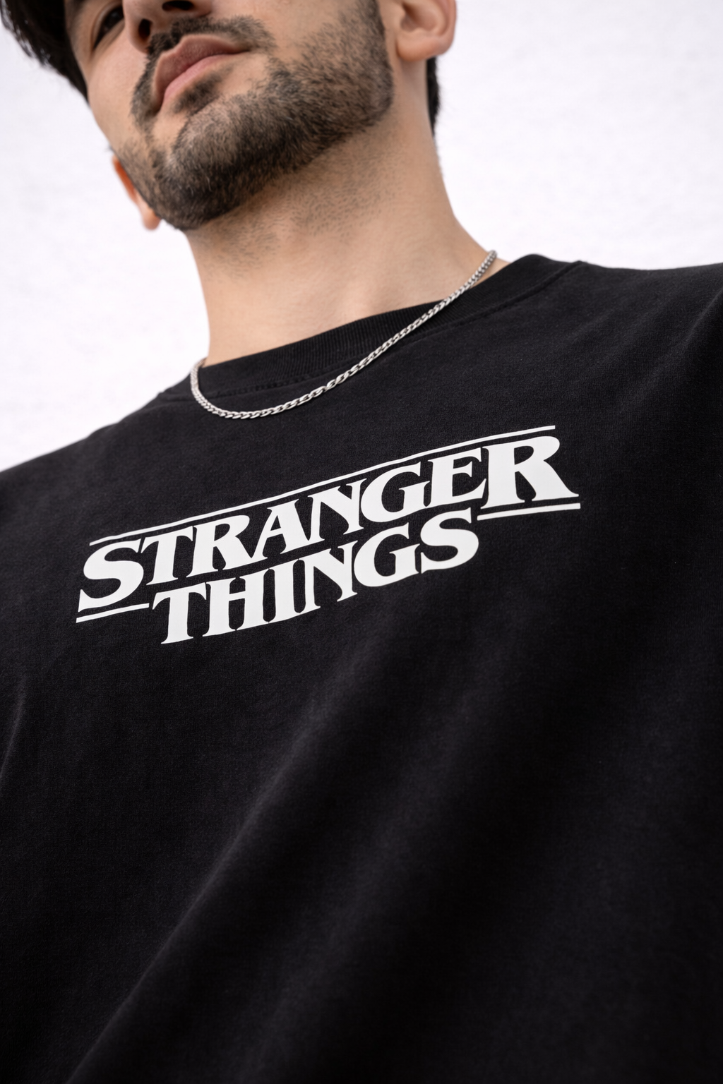 Two black 'Stranger Things' t-shirts on a textured surface with decorative items in the background.