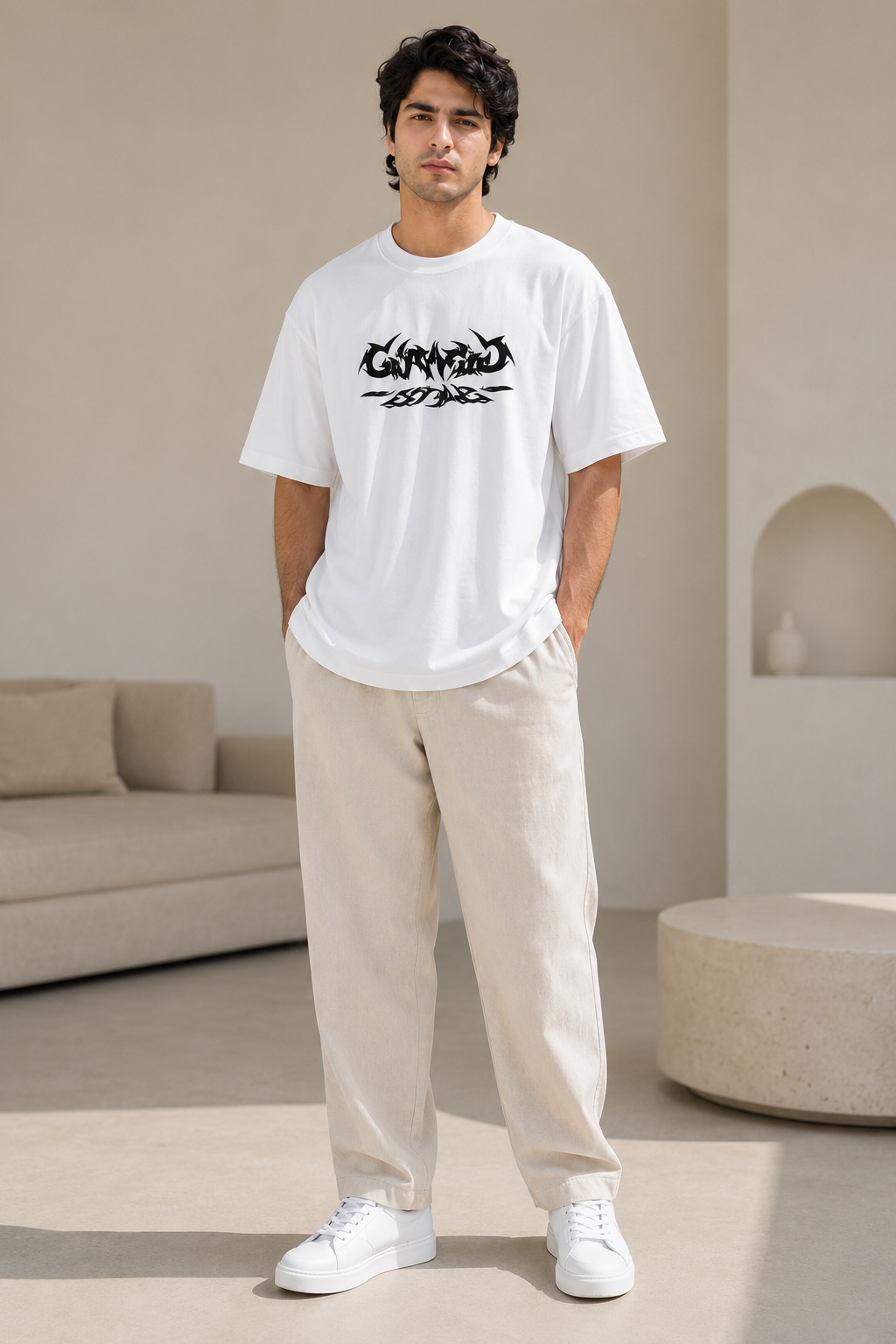 Man wearing a white t-shirt with black text and beige pants in a modern room.