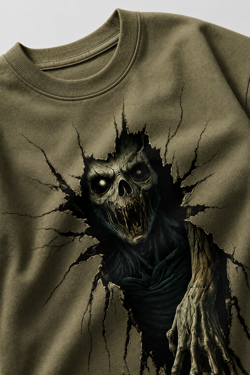 Close-up of olive green oversized graphic T-shirt showing detailed 3D horror skull print, fabric texture and ribbed crew neck.