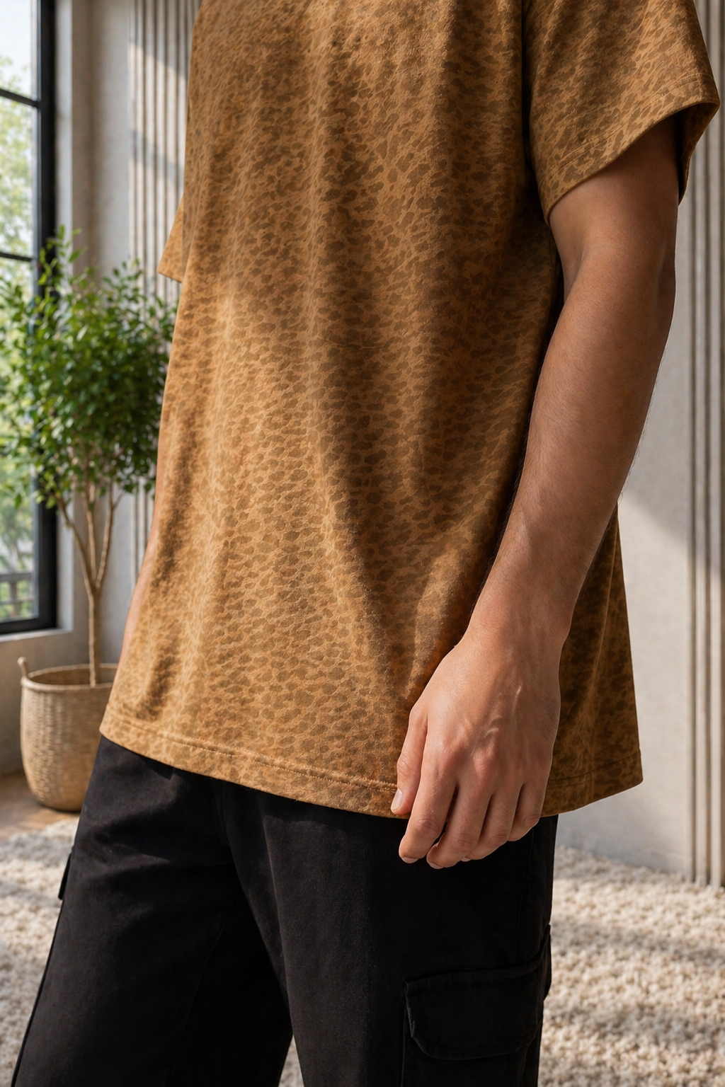 Person wearing a brown t-shirt and black pants in an indoor setting with plants and a window.