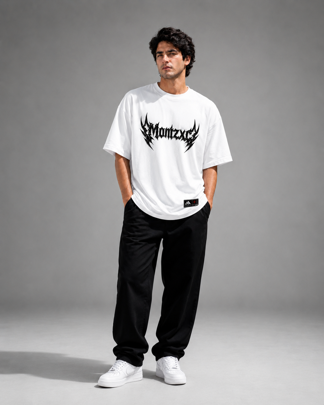 Man wearing a white t-shirt with a black logo and text, black pants, and white sneakers on a gray background